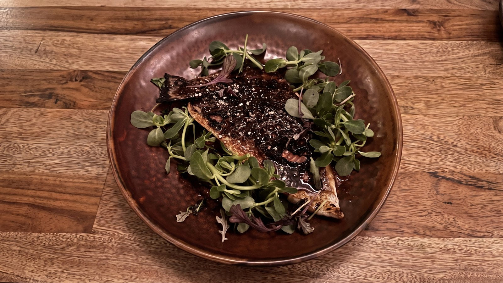 Glazed fish with greens on a copper plate